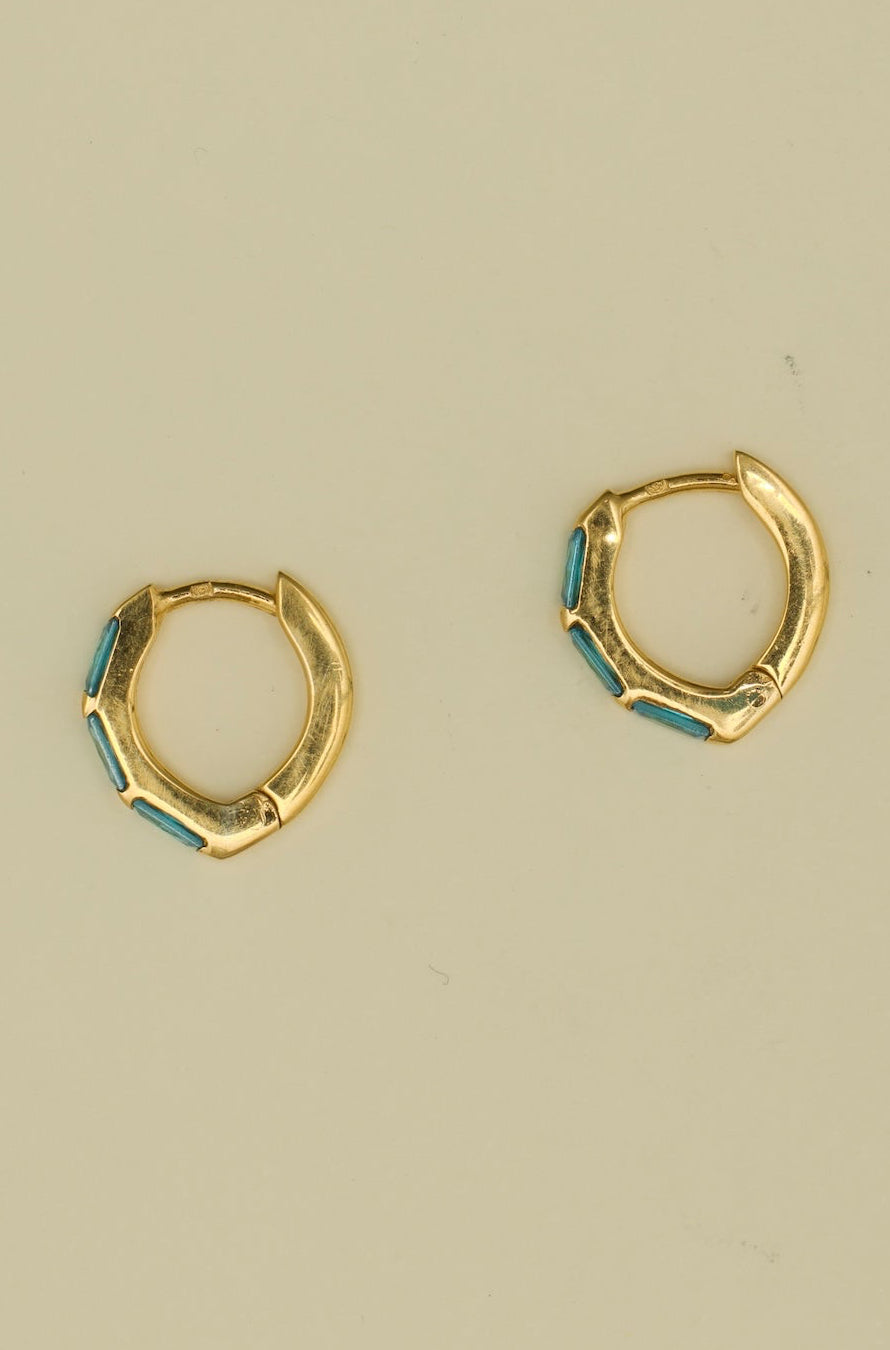 Gold hoop earrings with blue accents on a beige background