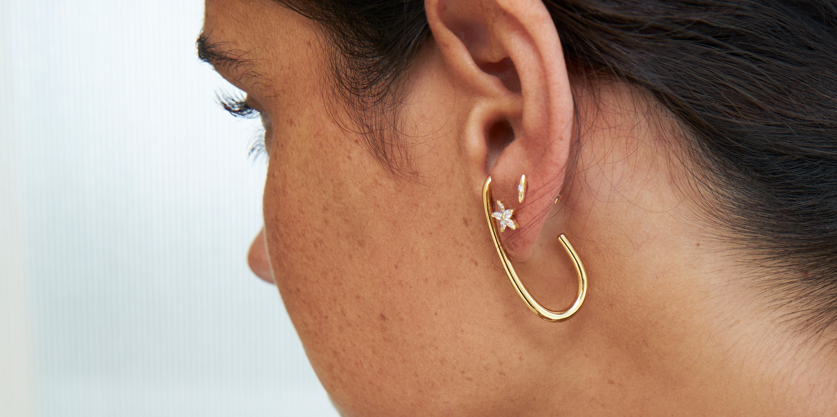 Close-up of a woman wearing gold hoop earrings and a pearl necklace against a blurred background.