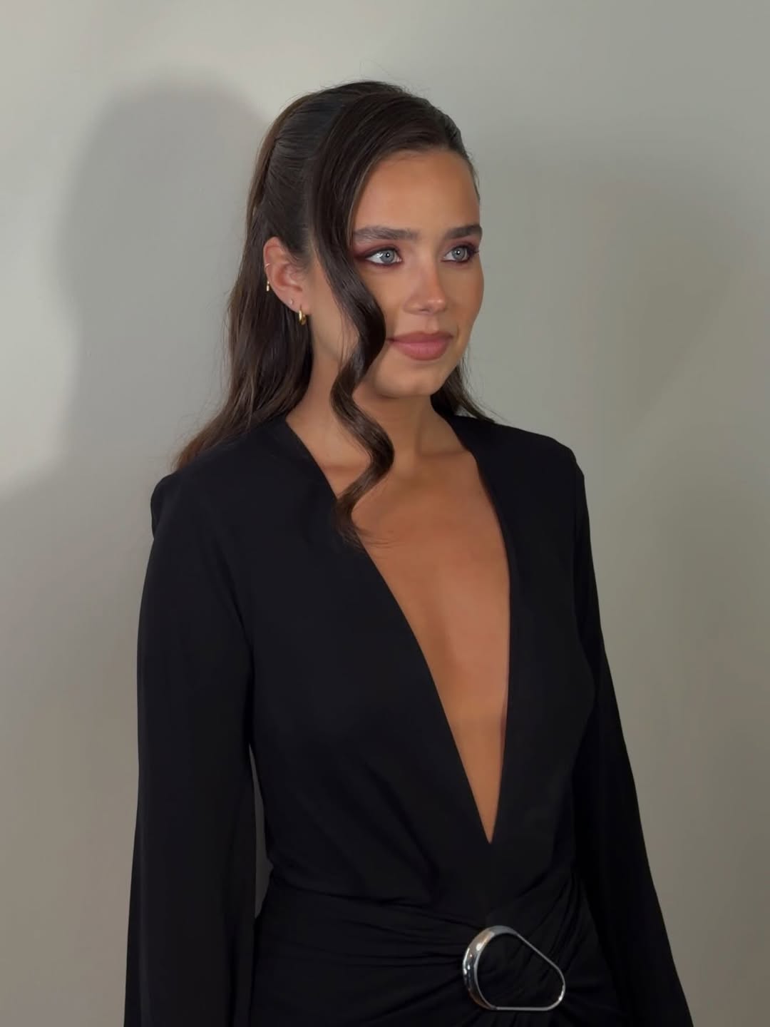 CINCO Jewelry model wearing a black deep V-neck dress with a stylish belt detail, side view image.