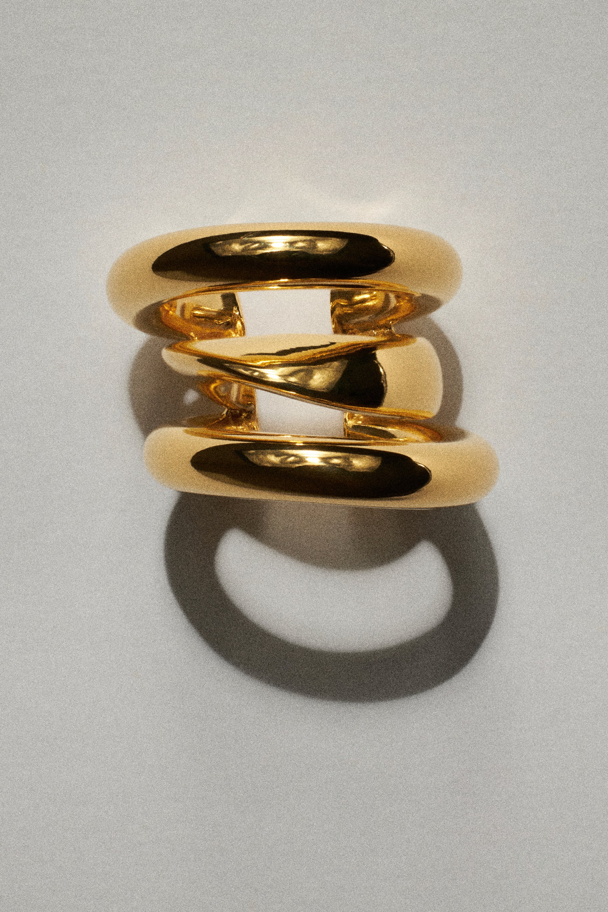 Gold earring with three interlocking bands on a light gray background