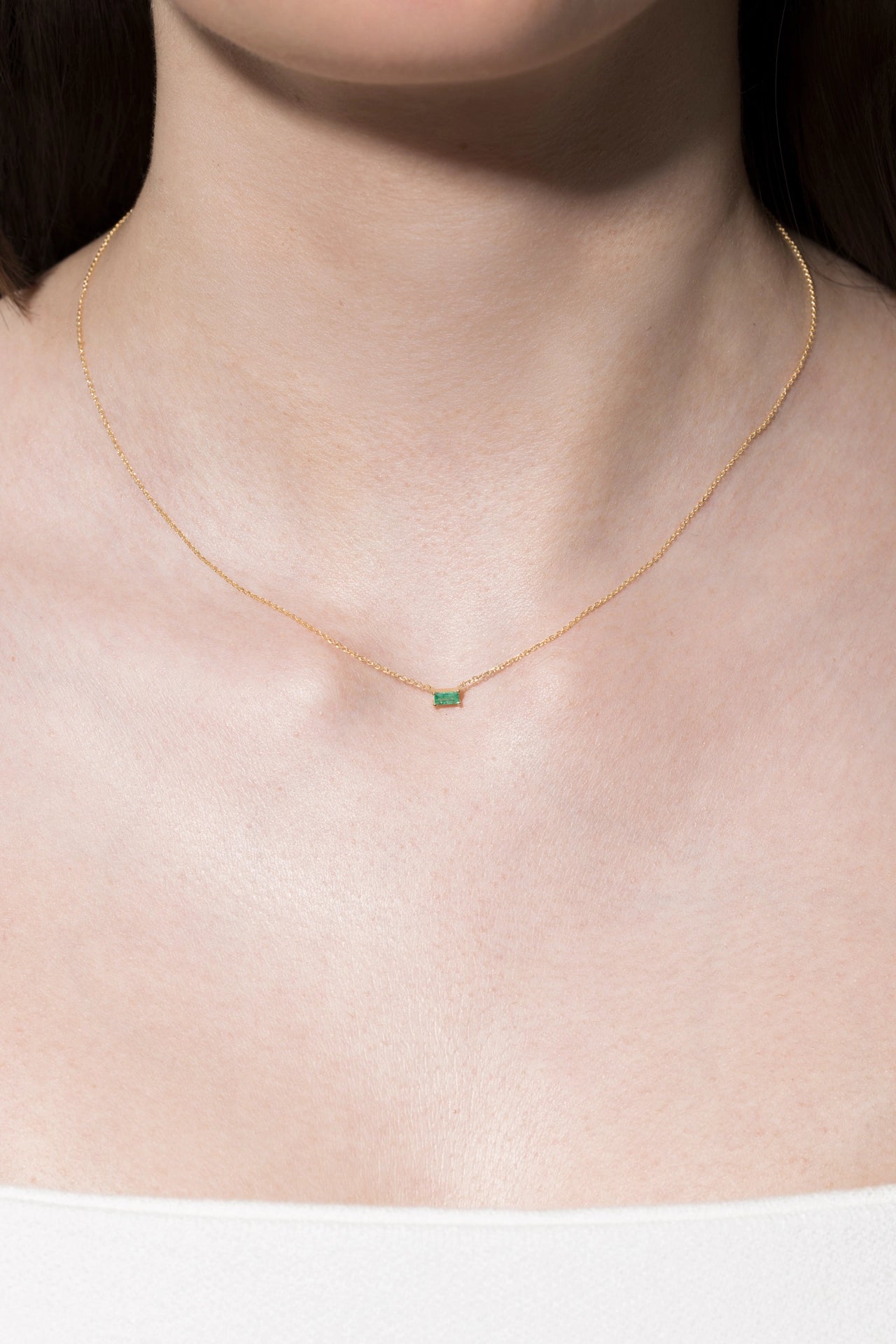 Gold necklace with a green gemstone on a person's neck