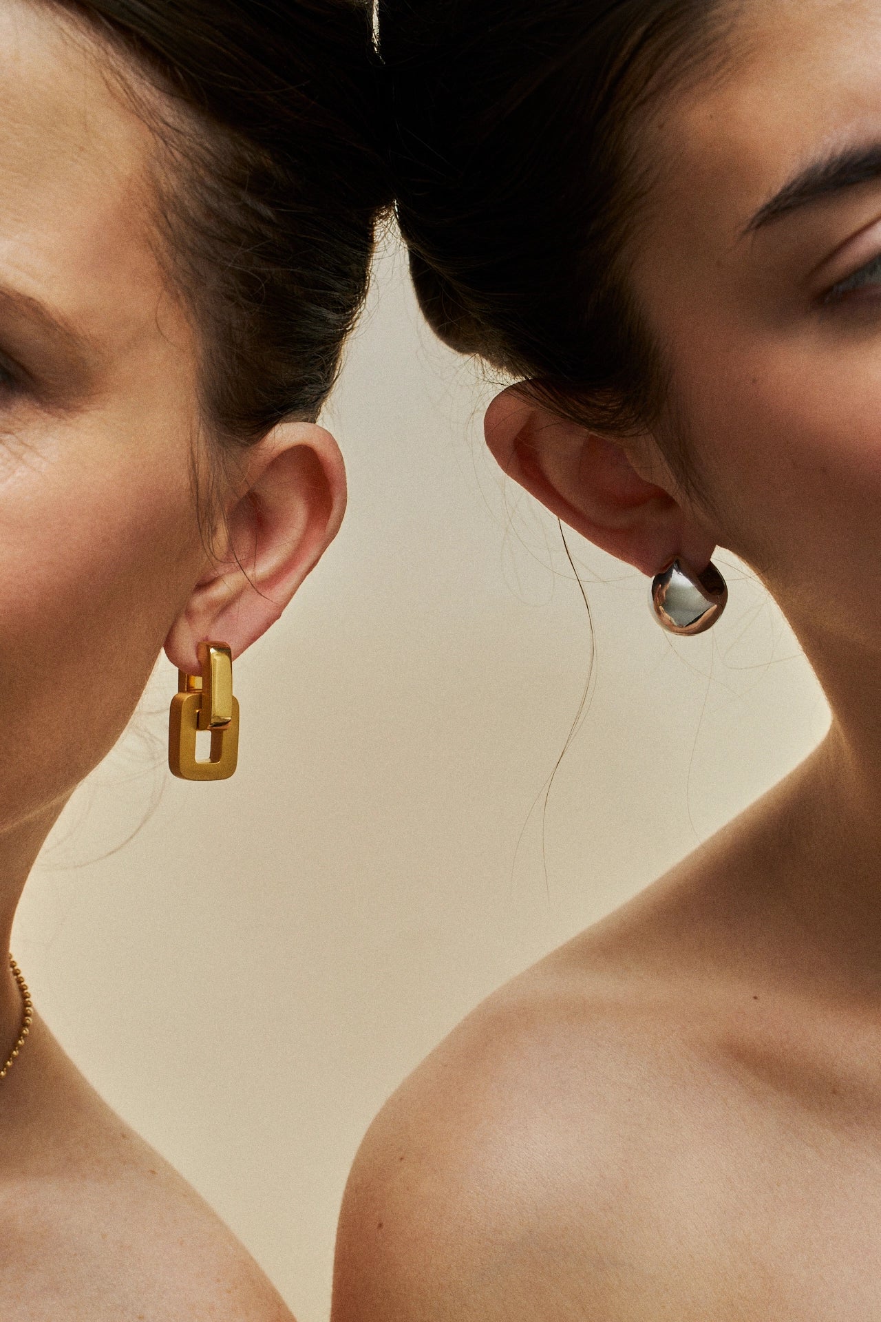 Two women wearing gold hoop earrings against a neutral background