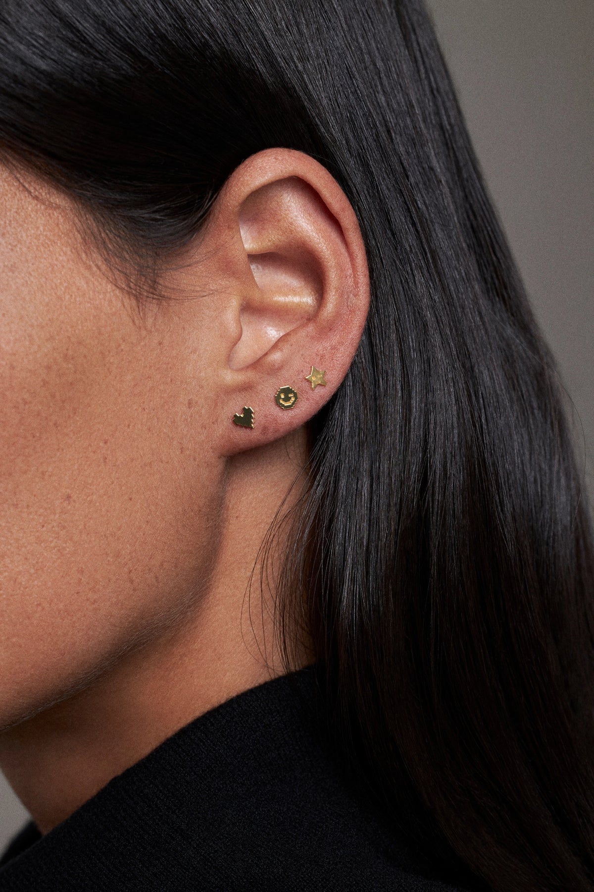 CINCO earring set with heart, smiley, and star studs worn on ear in a close-up view.